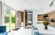 Bright interior of Taos XL Delux mobile home at Baalse Hei, Belgium, showing kitchen, dining area and garden view.
