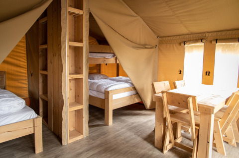 Interieur van een safaritent op Baalse Hei in België met houten meubels en stapelbedden.