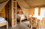 Interieur van een safaritent op Baalse Hei in België met houten meubels en stapelbedden.