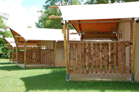 Safari tents at Baalse Hei in Belgium, featuring wooden decks and green grass under a sunny sky.
