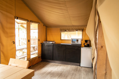 Vista interior de la cocina de una tienda safari en Baalse Hei, Bélgica, con estufa, microondas y mesa.
