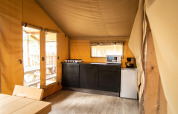 Vista interna della cucina di una tenda safari a Baalse Hei, Belgio, con fornello, microonde e tavolo.