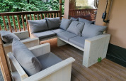 Gemütliche Sitzecke mit Holzsofas und grauen Kissen auf der Terrasse eines Safarizeltes bei Baalse Hei, Belgien.