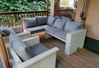 Salon extérieur avec canapés en bois et coussins gris dans une tente safari à Baalse Hei, Belgique.