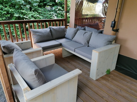 Outdoor patio with wooden sofas and grey cushions in a safari tent at Baalse Hei, Belgium, surrounded by greenery.