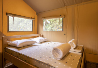 Zona notte nella tenda Safari Dreamer a Baalse Hei, Belgio, con letto matrimoniale, cuscini e finestre.