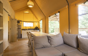 Interiør af Ranger Lodge safari-telt på Baalse Hei i Belgien med trægulv, åbent køkken og moderne sofa.