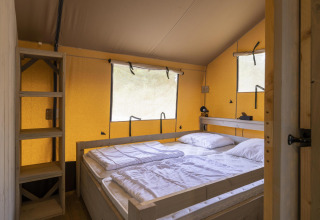 Soveværelse i en Ranger Lodge safariteltsuite på Baalse Hei, Belgien, med dobbeltseng og træhylder.