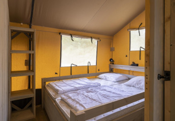 Soveværelse i en Ranger Lodge safariteltsuite på Baalse Hei, Belgien, med dobbeltseng og træhylder.