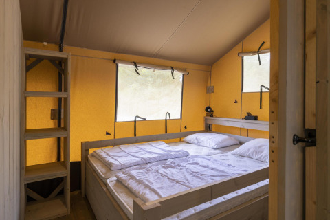 Dormitorio en tienda safari Ranger Lodge en Baalse Hei, Bélgica, con cama doble y estanterías de madera.