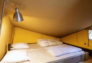Intérieur d'une tente safari à Ranger Lodge, Baalse Hei, Belgique, avec un lit double et une lampe de lecture.
