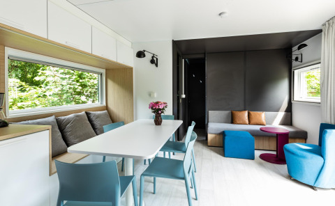 Moderna cabaña Taos XL en Petite Suisse, Bélgica, con comedor, sofá y ventanas grandes con vista natural.