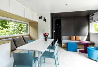 Moderna cabaña Taos XL en Petite Suisse, Bélgica, con comedor, sofá y ventanas grandes con vista natural.