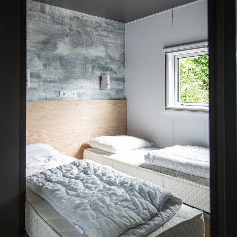 Et lyst værelse med to enkeltsenge, hvide sengetæpper og vindue, Taos XL lodge i Petite Suisse, Belgien.