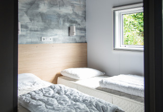 Et lyst værelse med to enkeltsenge, hvide sengetæpper og vindue, Taos XL lodge i Petite Suisse, Belgien.