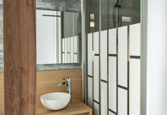 Baño moderno con lavabo redondo, espejo y ducha en la cabaña Taos XL de Petite Suisse, Bélgica.