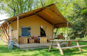 Glamping Sunshine en Petite Suisse, Bélgica, con terraza de madera, bancos y rodeado de naturaleza.