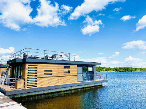 Casa flotante moderna en Vakantiepark Leukermeer, Países Bajos, con terraza y vistas al lago bajo un cielo azul.