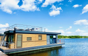 Casa flotante moderna en Vakantiepark Leukermeer, Países Bajos, con terraza y vistas al lago bajo un cielo azul.
