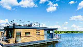 Casa flotante moderna en Vakantiepark Leukermeer, Países Bajos, con terraza y vistas al lago bajo un cielo azul.