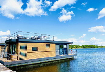 Casa flotante moderna en Vakantiepark Leukermeer, Países Bajos, con terraza y vistas al lago bajo un cielo azul.