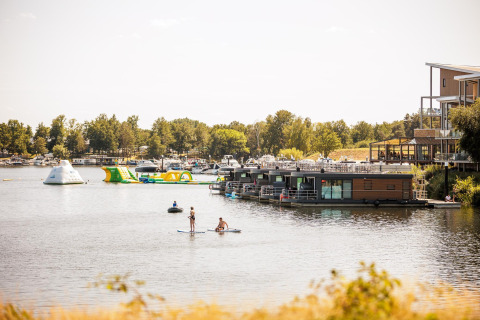 Flydende husbåd, folk på paddleboards, og vandlegetøj i sø ved Vakantiepark Leukermeer, Holland.