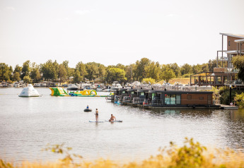 Casa flotante, personas en paddleboard y estructuras inflables en Vakantiepark Leukermeer, Países Bajos.