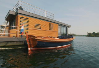 Moderne woonboot met houten gevel en aangemeerde sloep aan Vakantiepark Leukermeer in Nederland.