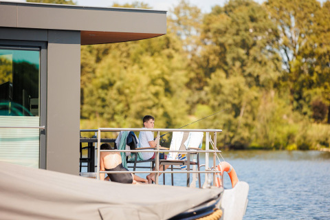Dos personas se relajan y pescan en la terraza de una casa flotante en Vakantiepark Leukermeer, Países Bajos.