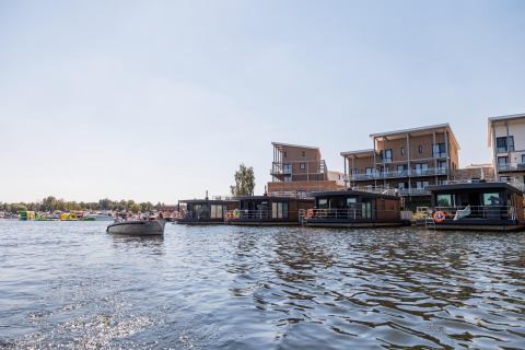 Casas flotantes en Vakantiepark Leukermeer, Países Bajos, con apartamentos modernos al fondo junto al agua.