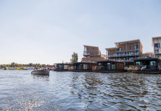 Casas flotantes en Vakantiepark Leukermeer, Países Bajos, con apartamentos modernos al fondo junto al agua.