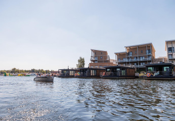 Casas flotantes en Vakantiepark Leukermeer, Países Bajos, con apartamentos modernos al fondo junto al agua.