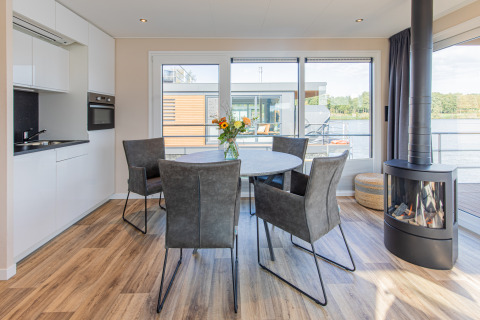 Zona de comedor moderna con chimenea y vista al lago en una casa flotante en Vakantiepark Leukermeer.