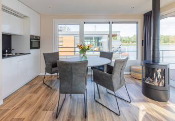 Zona de comedor moderna con chimenea y vista al lago en una casa flotante en Vakantiepark Leukermeer.