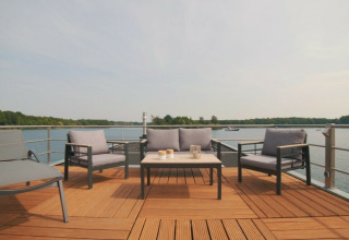 Zona de estar al aire libre en una casa flotante en Vakantiepark Leukermeer, Países Bajos, con vista al lago.
