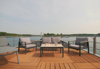 Zona de estar al aire libre en una casa flotante en Vakantiepark Leukermeer, Países Bajos, con vista al lago.