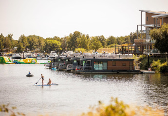 Vista del houseboat Floating House en Vakantiepark Leukermeer, Países Bajos, con personas en paddle surf.