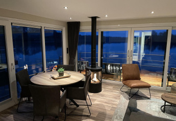 Moderne woonkamer met open haard op houseboat Floating House, Vakantiepark Leukermeer, Nederland, ’s avonds.