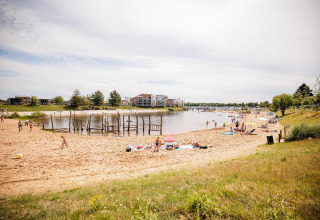Afbeelding van een zandstrand aan een lodge waar mensen ontspannen en spelen aan het meer op een zonnige dag.