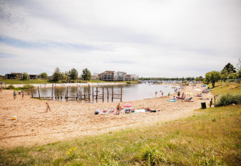 Foto de una playa de arena en un lodge con personas relajándose y jugando junto al lago en un día soleado.