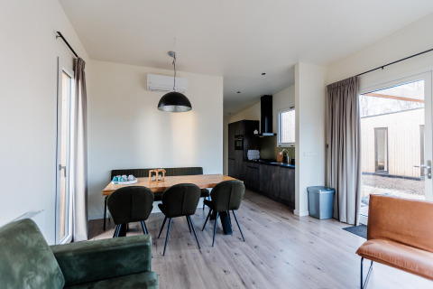 Salle à manger dans un lodge moderne, chaises vertes, lumière naturelle et cuisine ouverte élégante.