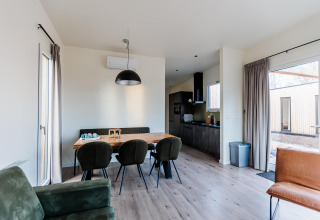 Eetruimte in een moderne lodge met groene stoelen en grote ramen, met een open keuken op de achtergrond.