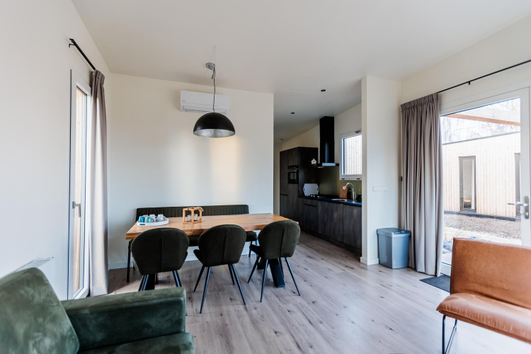 Moderne Lodge mit Essbereich, stilvollen Stühlen, großem Fenster und offener Küche im Hintergrund.