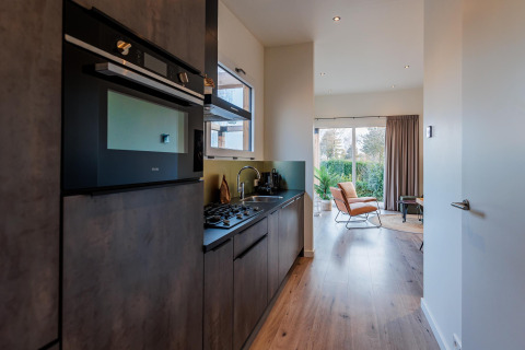 Cocina moderna en una lodge con electrodomésticos integrados y acceso a un luminoso salón con vistas al jardín.