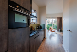 Moderne lodgekeuken met inbouwtoestellen, naast een lichtrijke leefruimte met zicht op het groen.