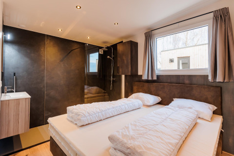 Dormitorio moderno con cama doble, ventana grande y baño privado en Beachlodge Deluxe en Vakantiepark Leukermeer.