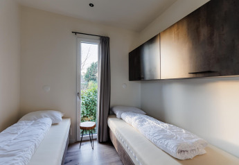 Piccola stanza in una lodge con due letti singoli, finestra stretta, pareti bianche e pensili scuri.