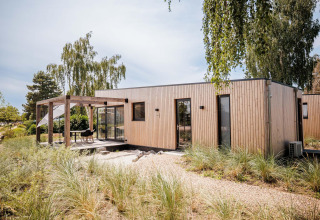Moderne Beachlodge Deluxe bij Vakantiepark Leukermeer, Nederland, met houten terras en beplanting.