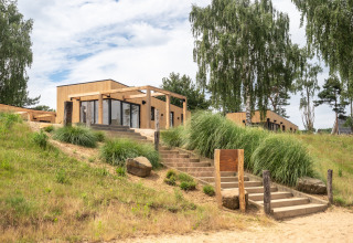 Buitenzicht op Beachlodge Deluxe in Vakantiepark Leukermeer, houten huisjes en groene natuur.