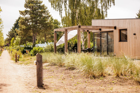 Extérieur du Beachlodge Deluxe au Vakantiepark Leukermeer aux Pays-Bas, terrasse en bois entourée d’arbres.